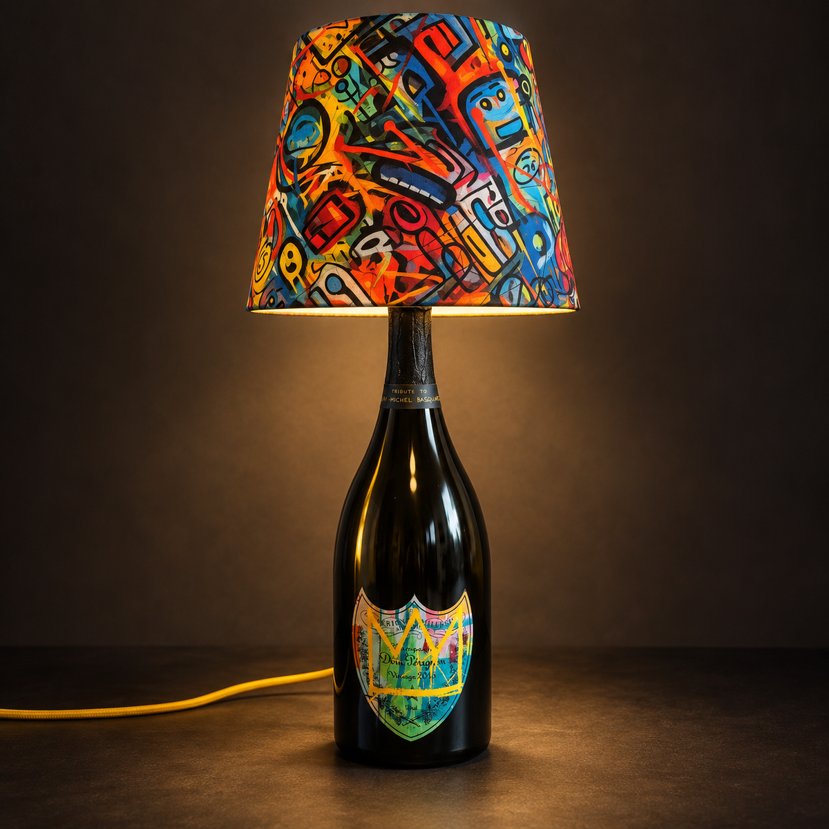 Yellow Basquiat bottle lamp switched on against a dark background.