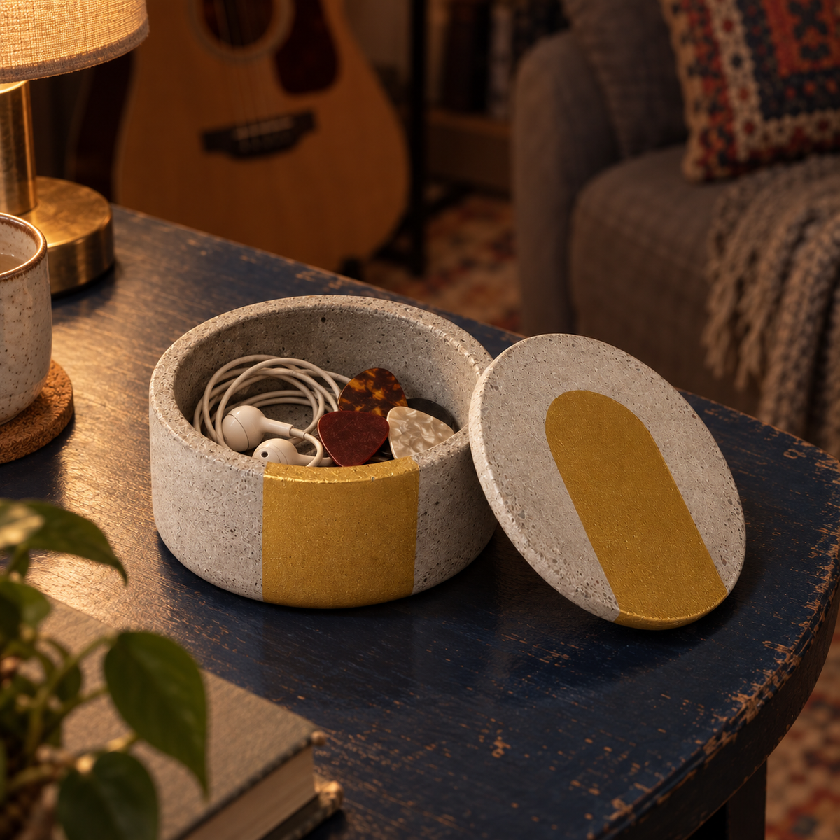 Smooth concrete canister with gold-tone band holding guitar picks and headphones in a living room