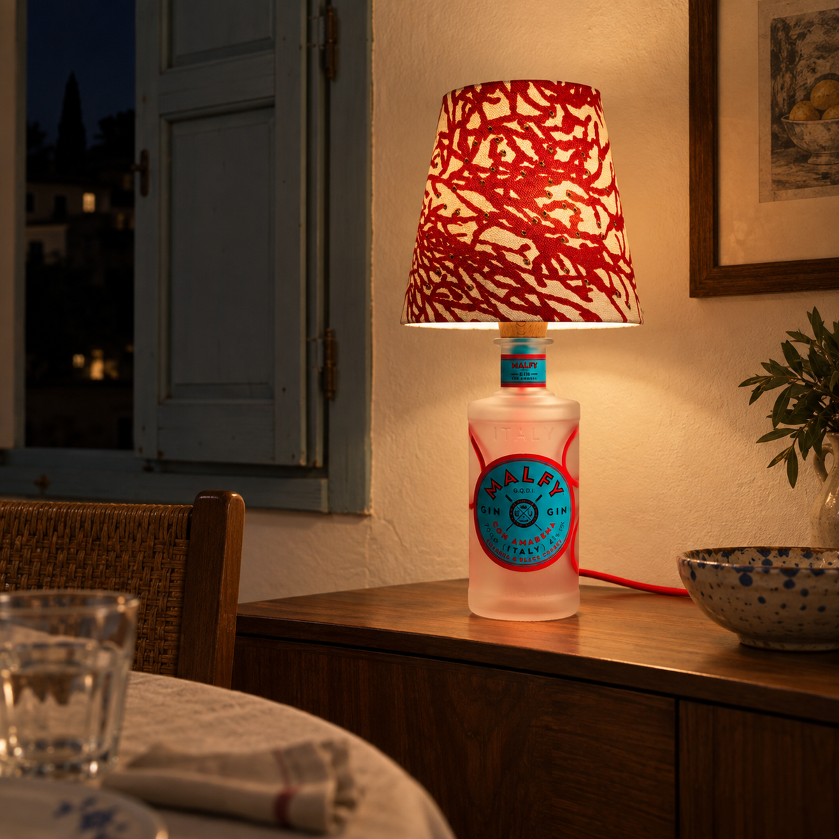 Malfy Con Amarena bottle lamp switched on on a sideboard in an Italian dining room at night