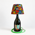 Bright product photo of the green-crown Dom Pérignon Basquiat bottle lamp with colorful fabric shade and green fabric-covered cord – AI-edited product image.