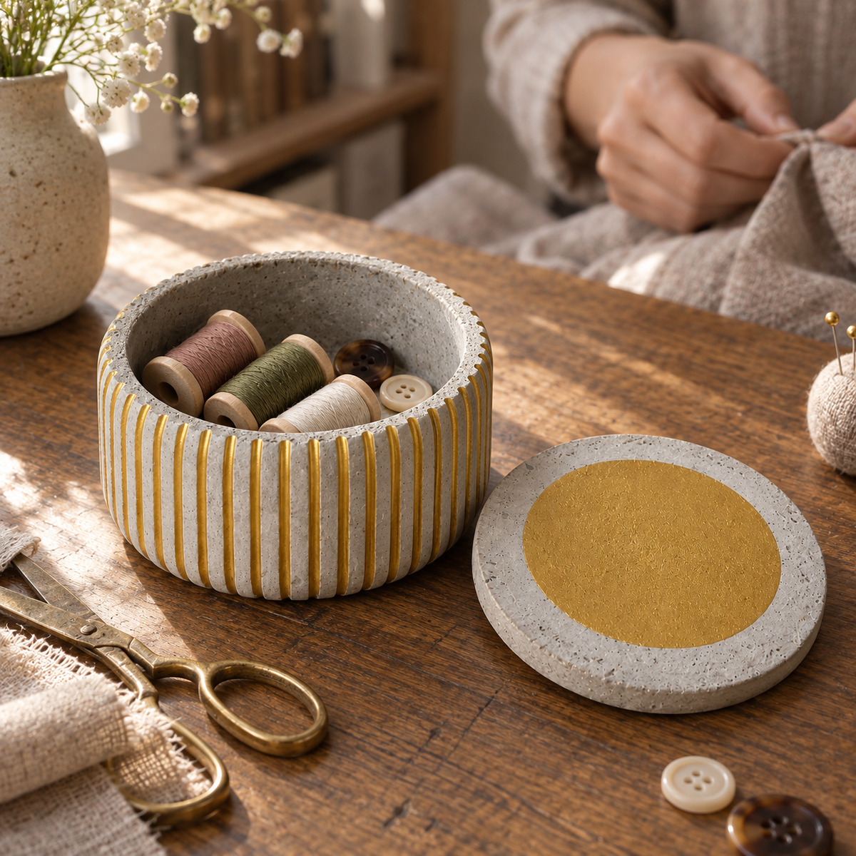 Fluted concrete canister with gold-tone lines used to store sewing supplies